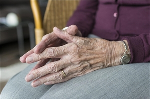 Das Foto zeigt die Hände einer alten Frau, die sie im Schoß faltet.