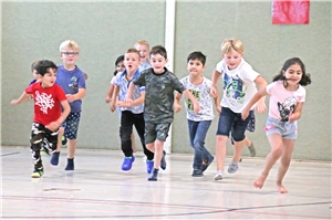 Ddas Foto zeigt eine Gruppe von Kindern, die in einer Turnhalle in die Kamera rennt.