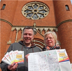 Marek Schirmer und Christine Henkel präsentieren den mehrsprachigen Witten-Stadtplan der Caritas vor der Kirche St. Marien. 