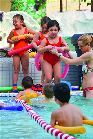 Unterstützt von einer Schwimmlehrerin, wagt das Mädchen Mirza mit einer Schwimmhilfe aus Schaumstoff den Schritt ins Schwimmbecken.