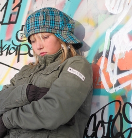 Eine traurige Jugendliche steht vor einer mit Graffiti bemalten Wand.