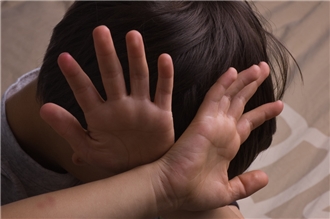 Ein dunkelhaariges Kind hält abwehrend die Hände vor den Kopf