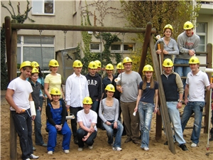 18 Personen mit gelben Bauhelmen stehen vor einer Schaukel in der Katholischen Kindertagesstätte St. Konrad in Berlin