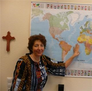 Wir können Frau Susanne Denzel auf dem Bild erkennen, sie steh vor einer Weltkarte.