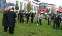 Die ersten Spatensticke wurden trotz Regen gemeistert. Es sind viele Leute mit Regenschirmen auf dem Bild zu sehen