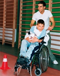 Ein junger Mann betreut einen körperlich behinderten Jungen, der im Rollstuhl sitzt.
