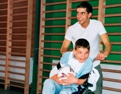 Ein behindertes Kind im Rollstuhl wird von einem jungen Mann betreut