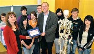 Schüler und die Leiterin der Berufsfachschule erhalten einen Scheck von Matthias Frahnow.