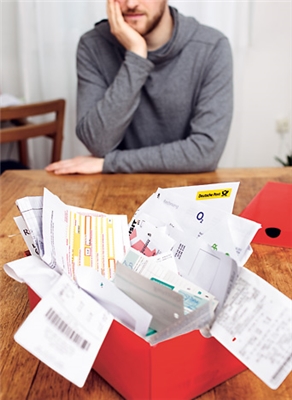 Mann blickt auf Schachtel mit ungeordneten Rechnungen (c) Simon Koy