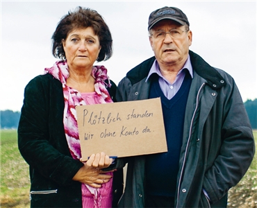Älteres Paar mit einem Karton in der Hand auf dem steht: Plötzlich standen wir ohne Konto da