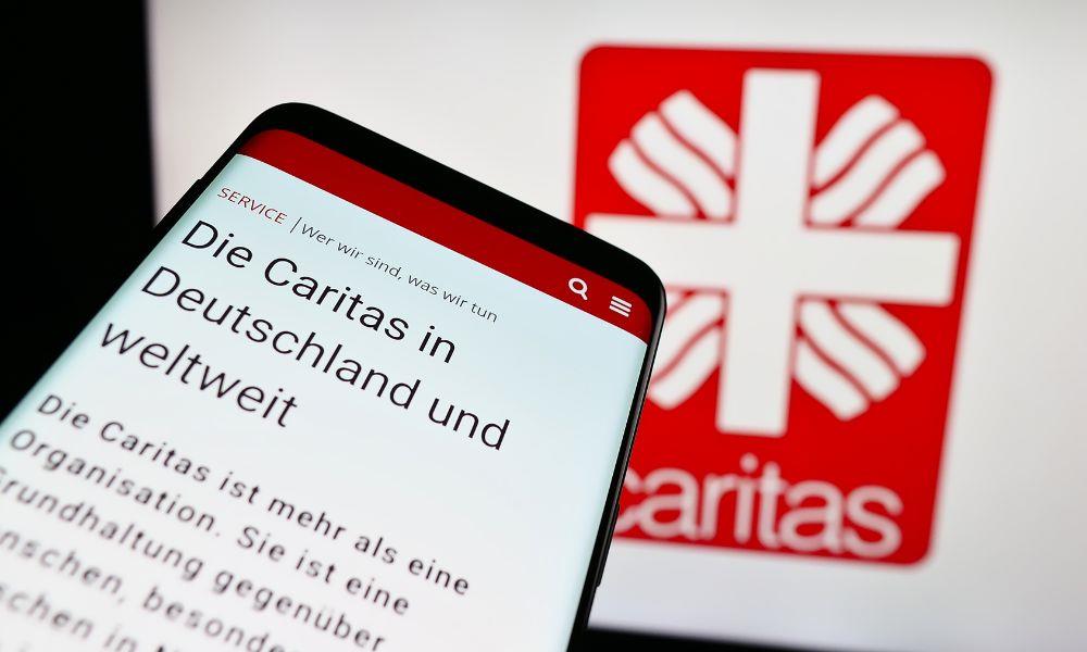 Mobiltelefon mit Caritasseite vor Wand mit Logo