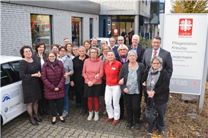 Einrichtungsleiterinnen Karola Sieger-Schmitz (links) und Sarah Bücker (3.v.l.) freuen sich mit ihren Teams, Vorständen und Gästen über die Eröffnung des neuen Standortes. Menschengruppe steht in der Einfahrt vor dem neuem Gebäude
