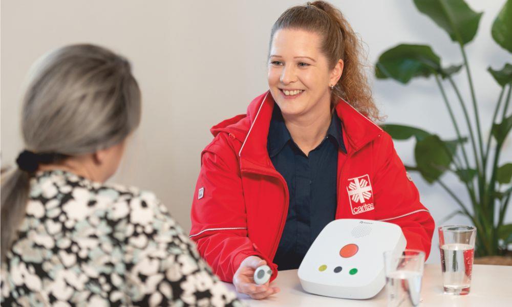 Caritas-Mitarbeiterin zeigt Seniorin Hausnotruftelefon