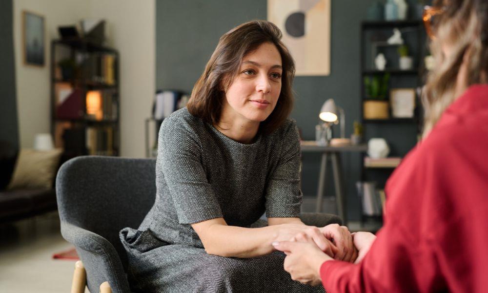 Zwei Frauen sitzend händehaltend einander gegenüber