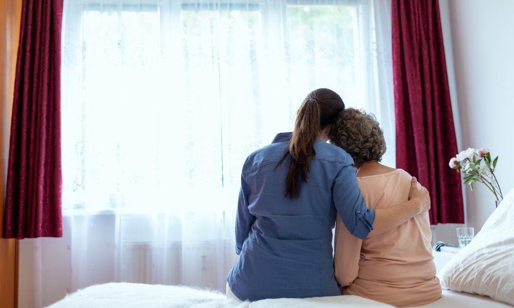 Frau umarmt Seniorin am Krankenbett