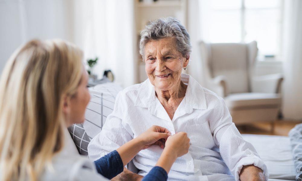 Pflegekraft hilt Seniorin beim Ankleiden