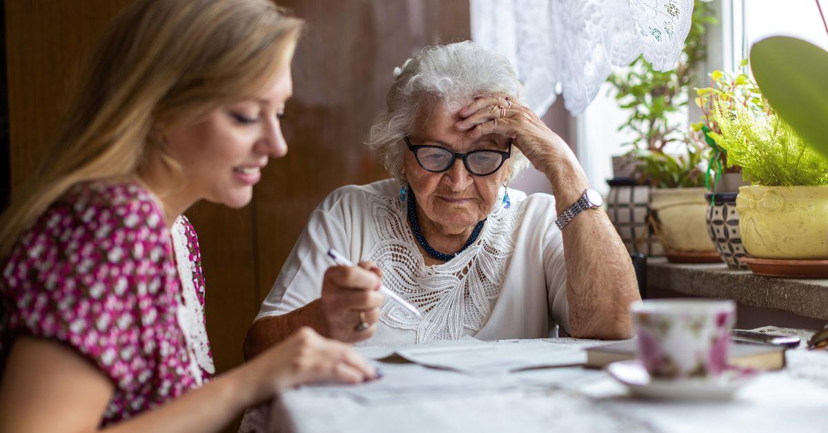 Junge Frau sitzt mit Seniorin am Tisch