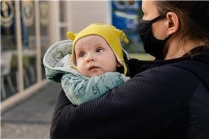 eine Frau mit Mundschutz hält ein Baby