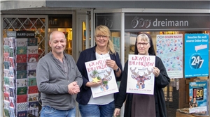 drei Menschen stehen für einem Buchladen und präsentieren Plakate der Wunschbaumaktion