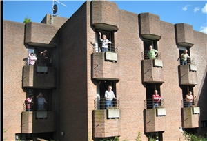 Hausansicht von außen, auf den Balkonen stehen die Bewohner und winken