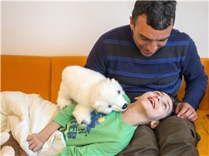 Behinderter Junge liegt auf den Knien eines Puppenspielers, der mit einem Eisbär aus Stoff spielt