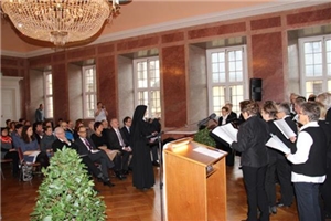 Wir sind zu Gast bei der Preisverleihung. Rechts im Saal haben sich Sänger eines Chores zusammengestellt. Eine Ordensschwester dirigiert sie. Links im Bild sitzen die Teilnehmer.