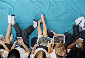 Kinder sitzen auf einer Matte und spielen mit Tablets