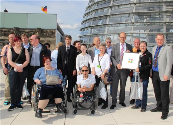 Vor der Glaskuppel des Bundestages  hat sich die Besuchergruppe der Caritas mit Michael Brand zusammen gefunden.  In der ersten Reihe sehen wir zwei Rollstuhlfahrer. Herr Brand und ein Werkstattratsmi