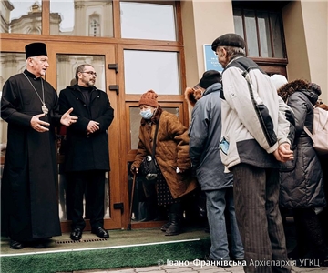 Der Bischof steht mit Bedürftigen vor einer Tür.