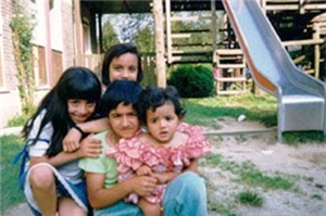 Vier Personen hocen eng zusammen. Es handelt sich wahrschienlich um eine türkische Mutter mit 3 Kindern.  Sie  befinden sich neben einem Haus auf einem Spielplatz.