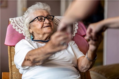 Eine Pflegerin hilft einer Seniorin beim Aufstehen aus dem Stuhl.