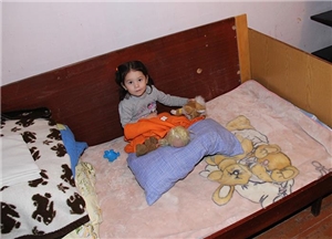 Ein junges Mädchen sitzt in einem bunt geschmückten Kinderbett und schaut uns an.