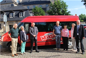 Die Delegierten haben sich vor der Abfahrt vor dem roten Fordbus der Caritas aufgestellt.