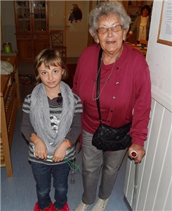Wir befinden uns in einer der Wohngruppen im Kinderheim in Fritzlar. Eine sehr rüstige Seniorin steht gestützt auf eine Gehhilfe, neben einem Kind. Beide schauen uns bewegt an.