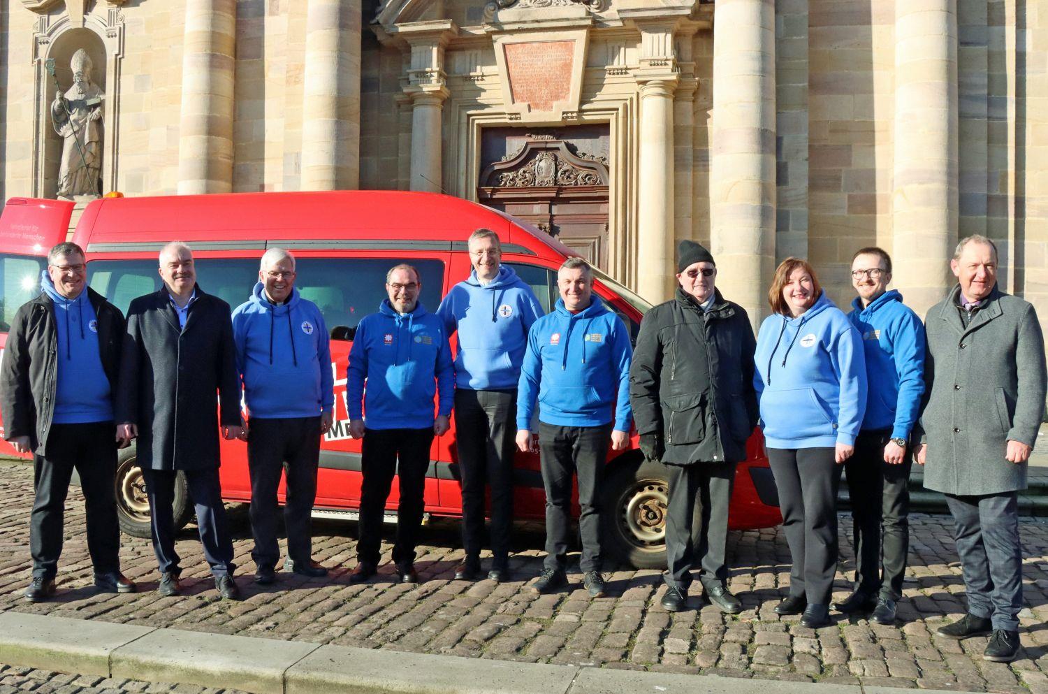 Eine Gruppe Menschen steht vor einem Transporter vor dem Dom