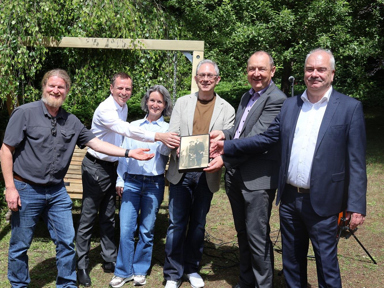 Mehrere Personen halten einen Bilderrahmen mit einem alten Foto eines Paares