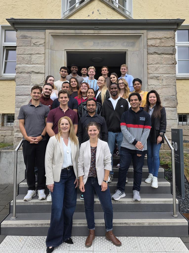Auf einer Treppe vor einem Gebäude stehen Studierende und Lehrende