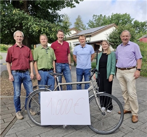 Mehrere Personen stehen um Fahrrad mit Spendenscheck