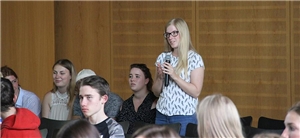 Eine Schülerin steht von ihrem Platz auf und spricht in ein Mikrofon.