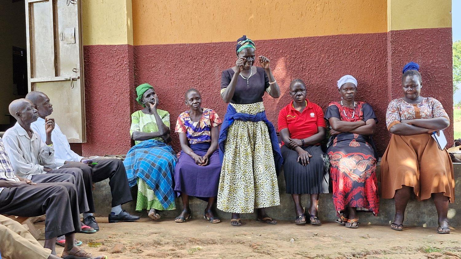 Eine Frau spricht in Uganda vor einer Hütte zu mehreren anderen Personen