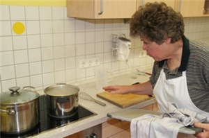 Eine Frau steht vor einem Küchenherd. In zwei großen Kochtöpfen sprudelt Wasser.