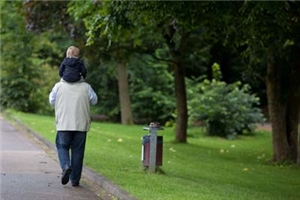 Ein �lterer Mann schlendert mit einem kleinen Kind auf den Schultern durch einen Park