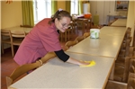 Eine Mitarbeiterin auf dem Bild wischt die Tische wieder sauber. Auch diese wichtige Tätigkeit fällt in den Aufgabenbereich der Hauswirtschaftsgruppe.