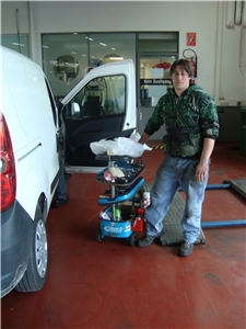 Der Mitarbeiter steht vor einem Fahrzeug in einem KFZ-Betrieb. Die Mithilfe bei den täglichen Aufgaben gehört zu seinen Tätigkeiten. 