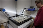 Auf dem Bild ist ein Mitarbeiter, der ein altes Buch mit einem großen Scanner (Blattgröße bis DIN A1) scannt.