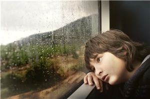 Kind schaut ans Fenster gelehnt aus dem Zug