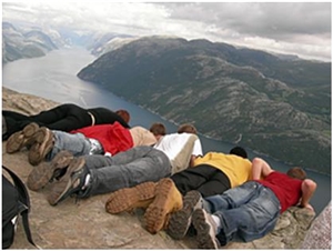5 Jugendliche liegen nebeneinander auf einem hohen Berg und blicken an einer Kante auf den tief liegenden See.