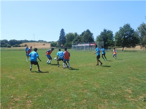 Bei sonnigem Wetter spielen Jugendliche unterschiedlicher Nationalität auf einem großen Sportplatz  gemeinsam Fußball.