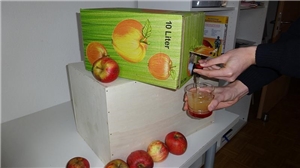 Nun wird aus einem Verpackten Behälter der frische Apfelsaft gezapft.