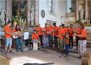 Die Jugendlichen aus der Wohngruppe haben sich mit roten T-Shirts und ihren Musikinstrumenten in der Kirche von Hilders vor dem Altar als Gruppe aufgestellt.